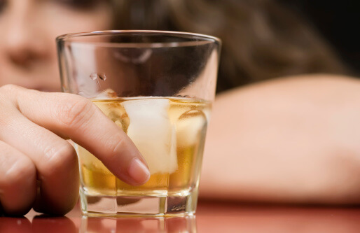 a woman stares at a glass of alcohol and thinks about alcohol addiction rehab