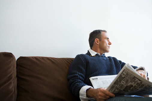 a man sits on a couch at an intensive outpatient program for substance use and reads the newspaper