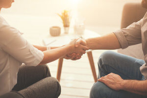 woman holds man's hand while she tells him about paying for rehab