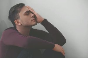 A man sits in a corner with his hand on his face as he struggles to define addiction