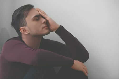 A man sits in a corner with his hand on his face as he struggles to define addiction