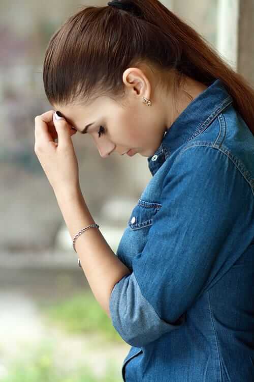 A woman looks down resting her forehead on her hand as she goes through painkiller withdrawal symptoms