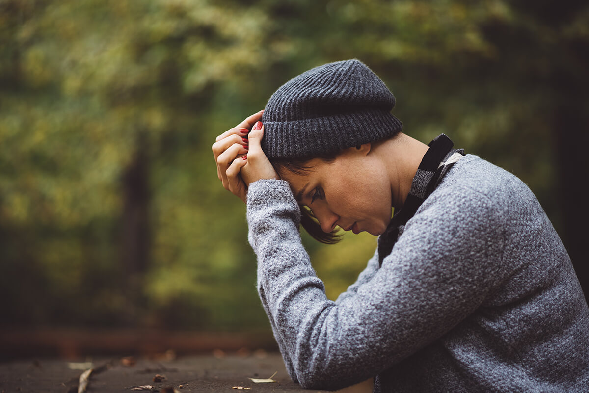 stressed woman sitting in the woods worrying about the addiction cycle