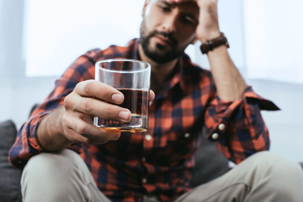 young man holds a glass of liquor as he wonders if he is developing an alcohol dependence