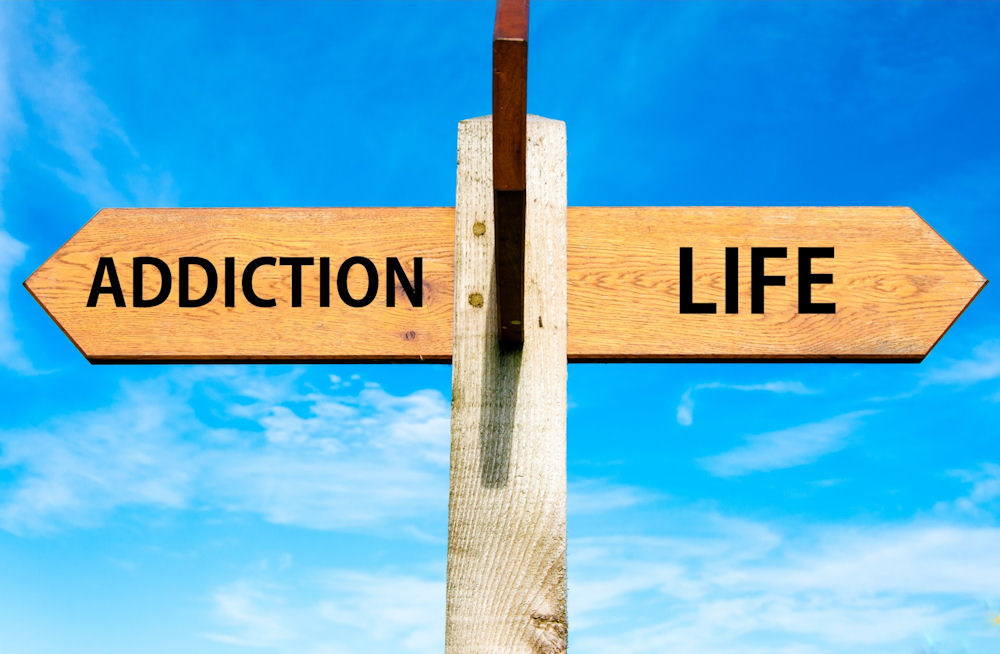 wooden sign with arrow labeled addiction pointing back and an arrow labeled life pointing forward