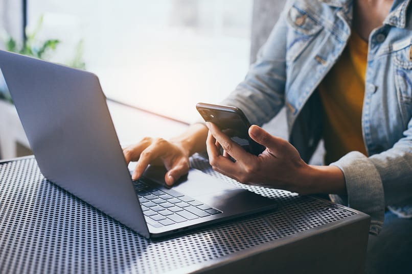 person on their laptop with phone in hand to contact rehab center