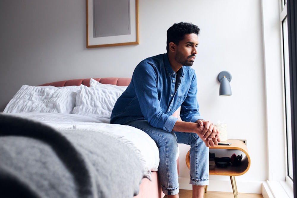 man sitting alone on edge of his bed