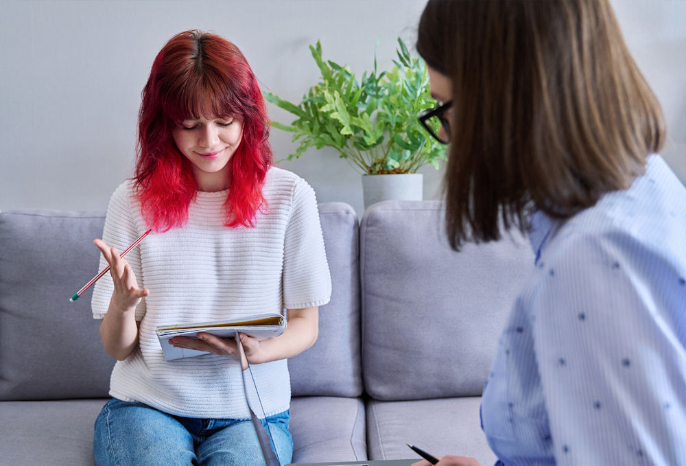 young woman sitting on a couch with a notebook, speaking with counselor