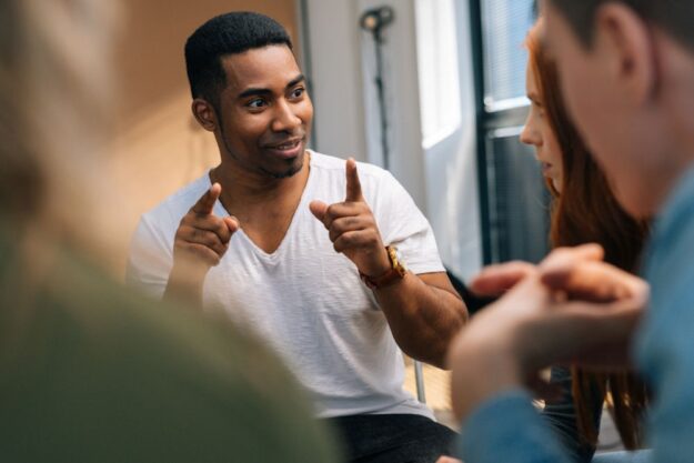 man holding hands up during discussion while addressing a group