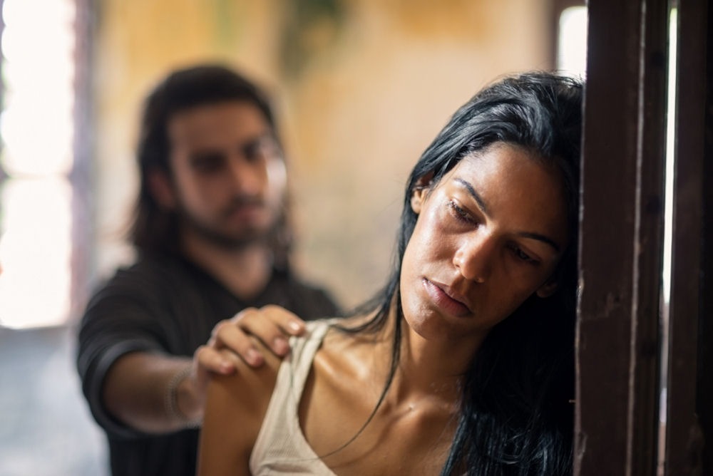 sad woman leaning in doorframe while partner puts hand on her shoulder