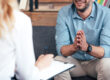 man folding his hands while talking to therapist who is taking notes