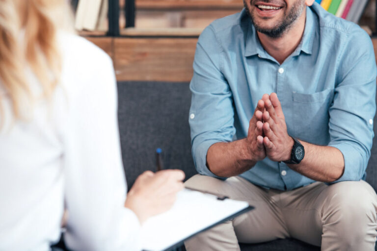 man folding his hands while talking to therapist who is taking notes