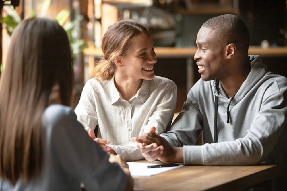 a couple looking at each other and smiling while they sit at a table with a third person